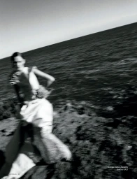Model wearing a light dress moving across a rocky coast with the ocean behind in a black and white editorial shot.