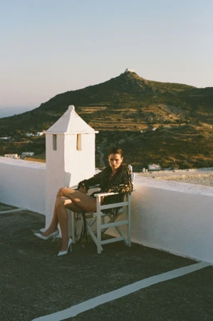 Model Dominika Drozdowska seated in a white director chair on an outdoor terrace with rolling hills in the background.