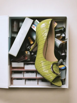 Chartreuse embossed open-toe high heel resting inside an open box filled with 35mm film rolls, slides, and photographic accessories.