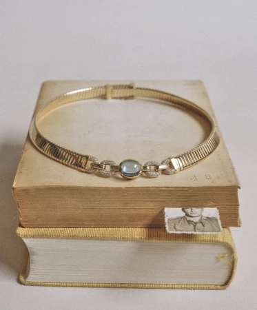 Gold collar necklace with a blue gemstone resting on a stack of vintage hardcover books with an old photograph bookmark.