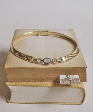Gold collar necklace with a blue gemstone resting on a stack of vintage hardcover books with an old photograph bookmark.