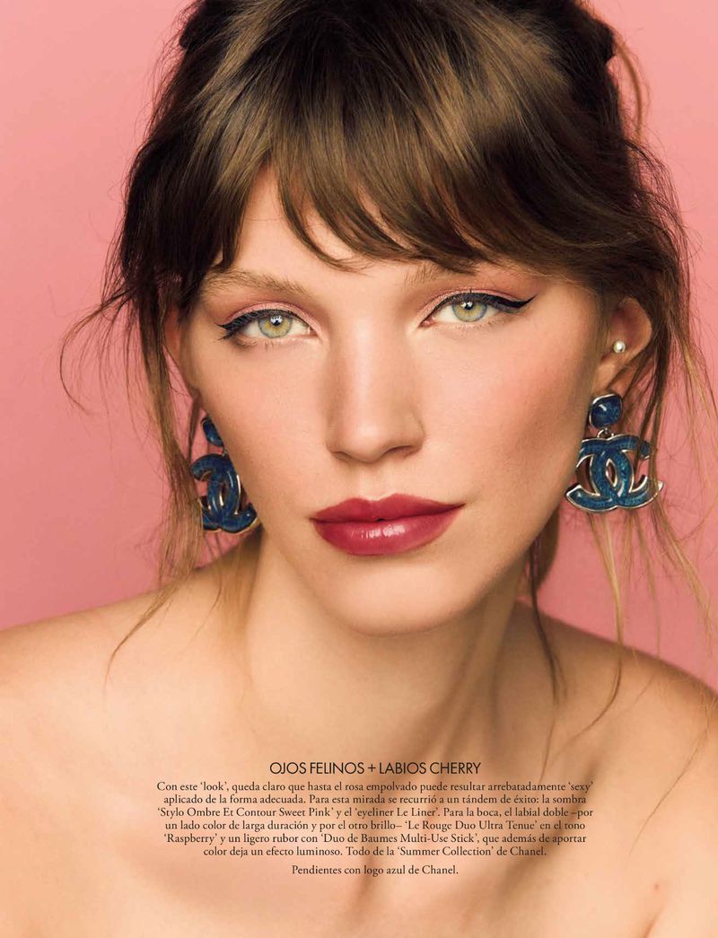 Close-up beauty portrait of Antonia El Ghali featuring winged eyeliner, berry lips, and blue Chanel earrings against a pink background.