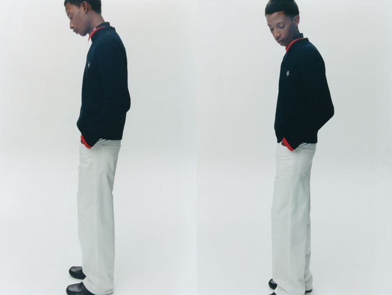 Two side-by-side shots of a young Black man standing in a black sweater with red trim, wide-leg off-white trousers, and black shoes.