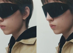 Model in black Loewe shield sunglasses, black hoodie, and tan suede jacket shown in side profile against a pale studio backdrop.