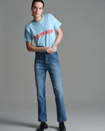 Model Charlotte Tomas wearing a light blue FATHER graphic t-shirt and blue straight-leg denim jeans against a grey studio backdrop.