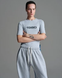 Model Charlotte Tomas wearing a grey 1980 t-shirt and matching sweatpants against a grey studio background for BETTTER.