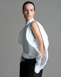 Model Charlotte Tomas wearing a deconstructed white cutout shirt and black trousers against a neutral grey studio background.