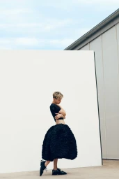 Troye Sivan standing outdoors wearing a black top and a voluminous textured black skirt for Vogue Australia.