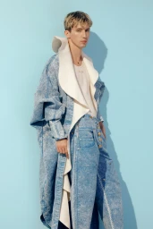 Troye Sivan wearing a blue denim coat with an oversized white collar and matching denim trousers against a light blue backdrop.