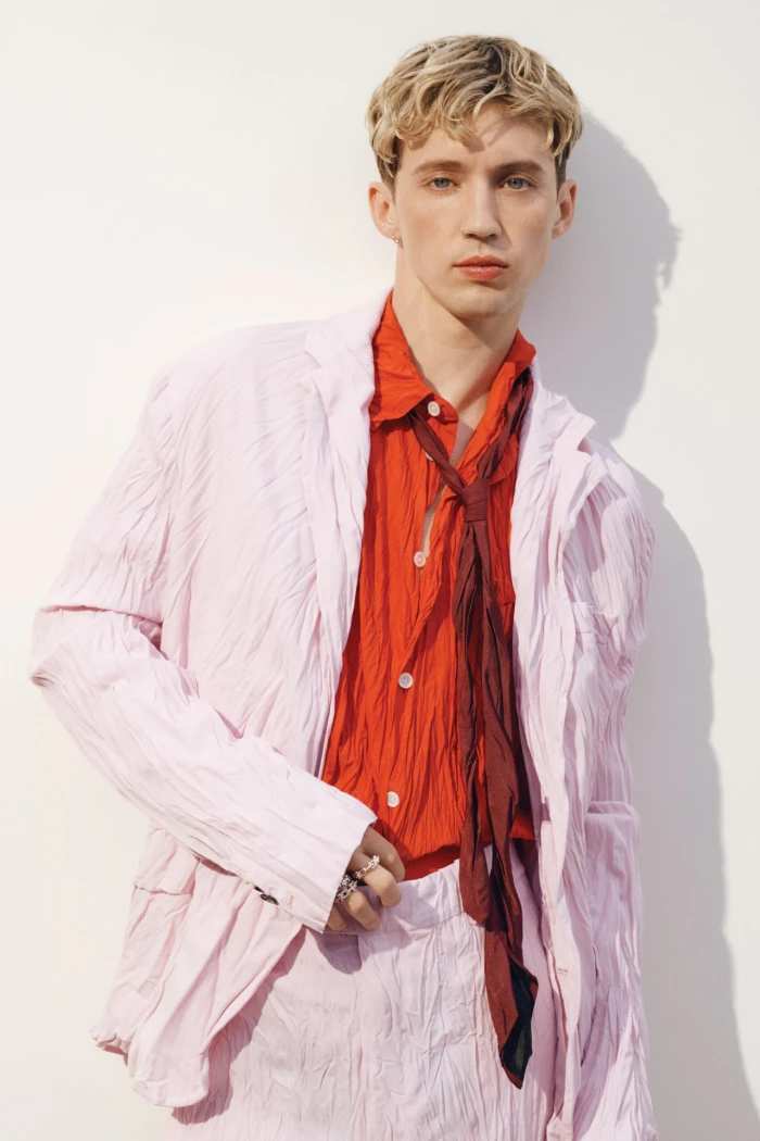 Troye Sivan wearing a light pink jacket and vibrant red shirt against a plain white background for Vogue Australia.