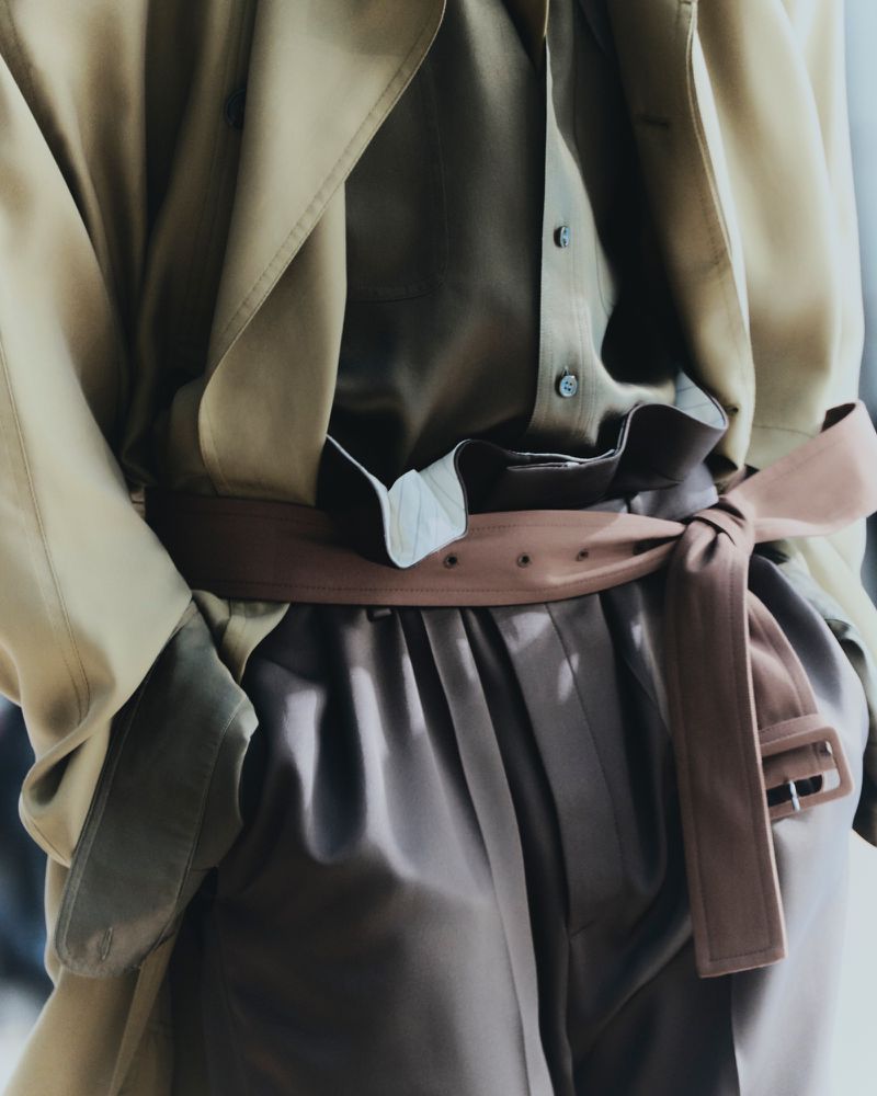 Fashionable tan trench coat with a brown belt, paired with a light-brown blouse and brown pants, creates a coordinated monochromatic look.