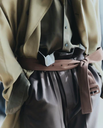 Fashionable tan trench coat with a brown belt, paired with a light-brown blouse and brown pants, creates a coordinated monochromatic look.