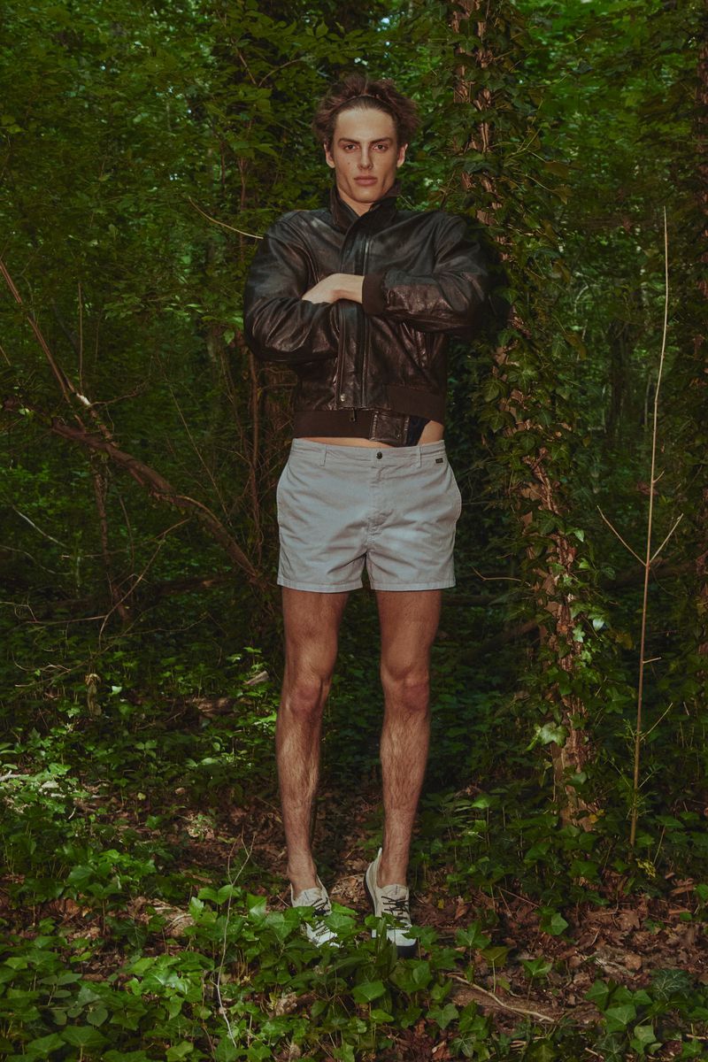Model Esteban Monbaliu wearing a dark leather jacket and grey shorts in a dense forest for El Pais Icon Magazine.