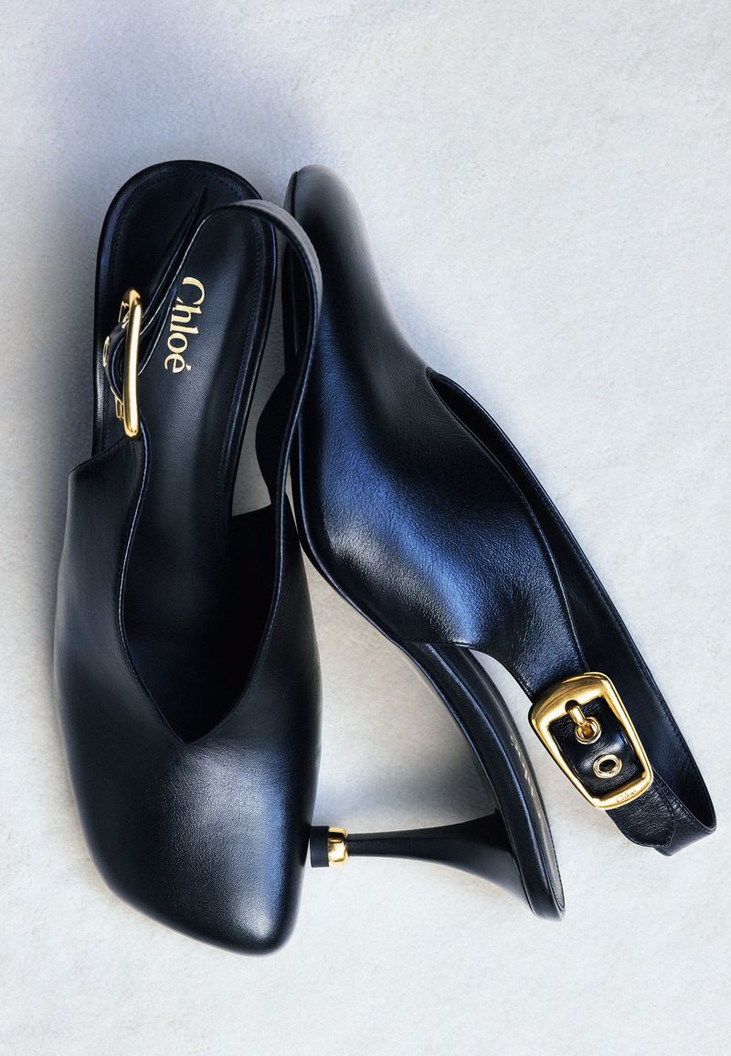 Close-up of black leather slingback heels with gold buckle, designer footwear, and stylish fashion accessories on a white surface.