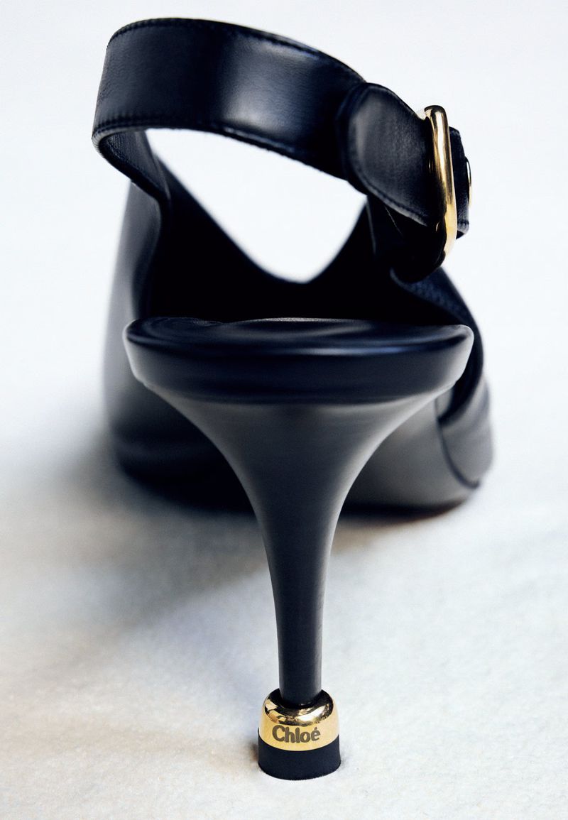 Studio shot of a black leather slingback heel with a stiletto heel and a gold buckle, the Chloe logo visible near the bottom of the heel.