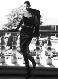 Mariacarla Boscono in a black dress, leather gloves, and boots standing on a stone balcony with a balustrade for Ermanno Scervino.