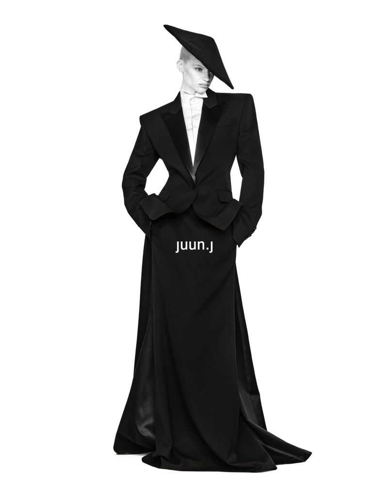 Mila van Eeten in a black structured tuxedo jacket, floor-length skirt, and angular hat against a white background for Juun.J.