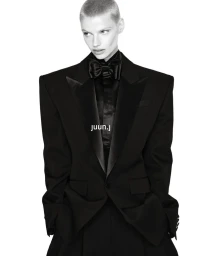 Model with a buzzcut wearing an oversized black tailored tuxedo jacket and bow tie against a white background for Juun.J F/W26