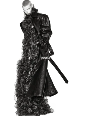 Model Mila van Eeten poses in an oversized black leather trench coat over a voluminous ruffled black dress on a white background.
