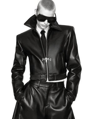 Mila van Eeten wearing a structured black leather jacket, dark sunglasses, and a tie against a seamless white background.