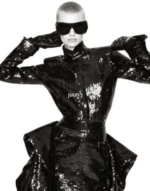 Model Mila van Eeten wearing a structured black sequin dress, dark oversized sunglasses, and leather gloves against a white studio backdrop.