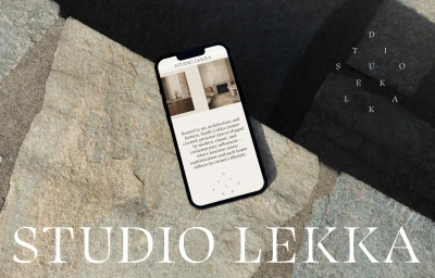Smartphone displaying the Studio Lekka mobile website resting on a textured stone surface with sharp diagonal shadows.