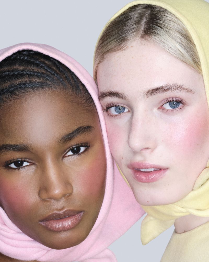 Close-up portrait of two models wearing pastel pink and pale yellow headscarves with rosy blush makeup on a neutral background.