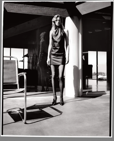 Black and white portrait of a model in a dark halter dress and polka dot tights standing in a modern interior.
