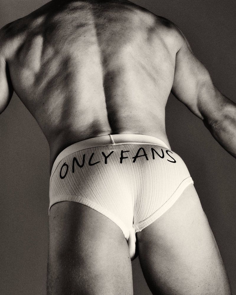 Rear view of a muscular man wearing white ribbed briefs featuring ONLYFANS text across the seat.