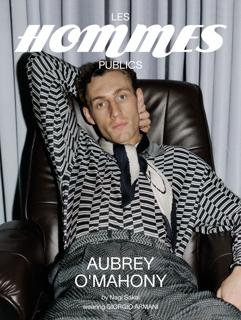 Aubrey O'Mahony seated in a brown leather armchair wearing a patterned black and white knit sweater for Les Hommes Publics.