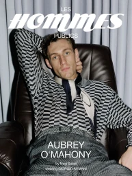 Aubrey O'Mahony seated in a brown leather armchair wearing a patterned black and white knit sweater for Les Hommes Publics.