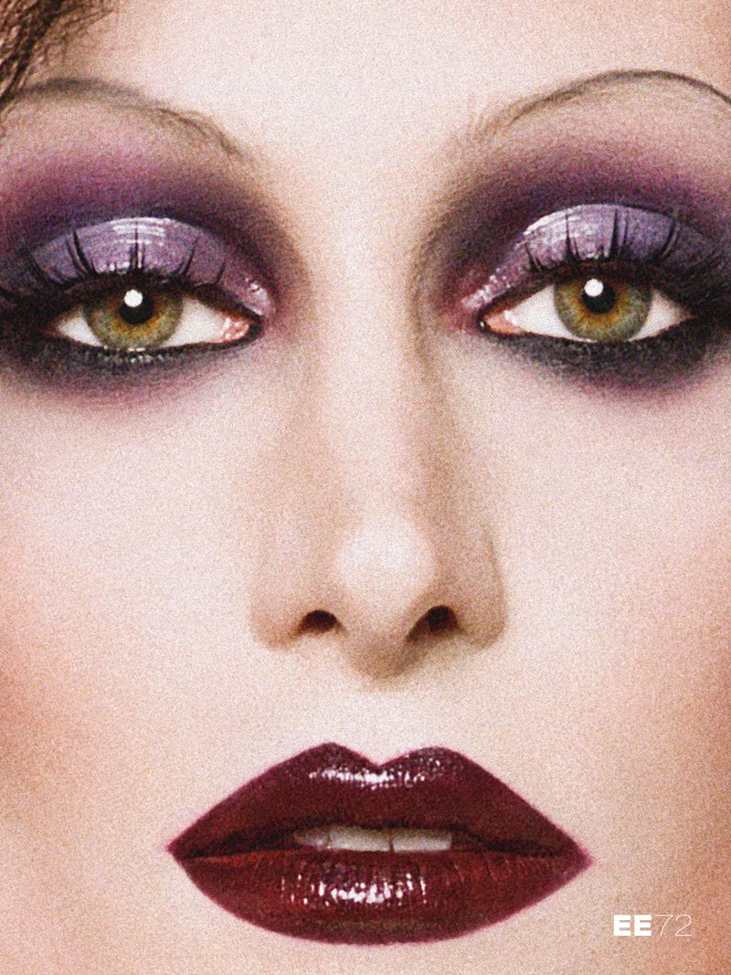 Close-up beauty portrait of a woman with glossy purple smokey eyeshadow, thin arched eyebrows, and dark glossy burgundy lipstick.