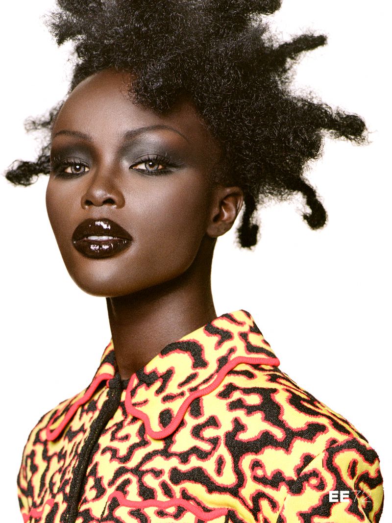 Model Anok Yai with dramatic dark glossy lips and sculptural hair against a white backdrop for 72 Magazine.