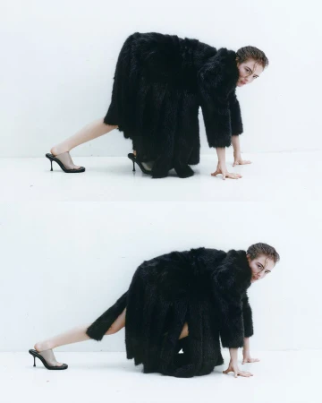 Model Stella Jones crouching in an oversized black textured coat and black high-heeled mules against a bright white seamless background.