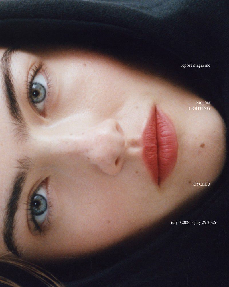 Close-up portrait of a woman wearing a black hood, featuring red lipstick and blue eyes, shot by Jacq Harriet for Report Magazine.