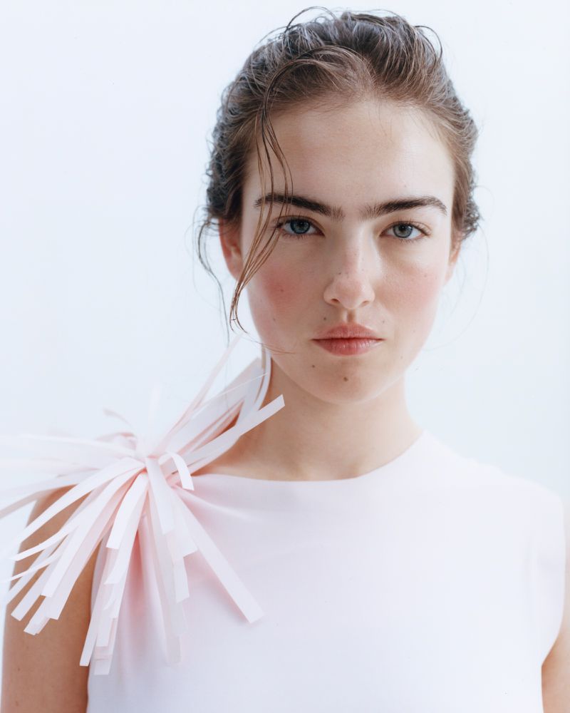 Model Stella Jones wearing a pale top with fringe shoulder detail against a bright white background.