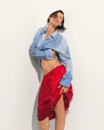 Model Bianca Balti wearing a wet blue button-down shirt and red skirt against a white wall for Harper's Bazaar Turkey.