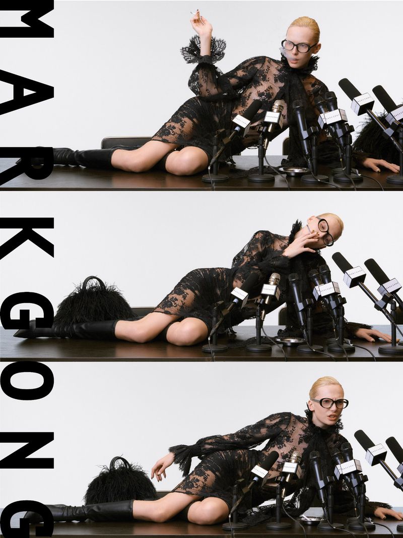 A model in a black lace dress lies on a table covered with microphones in a studio environment, exuding a retro fashion style.