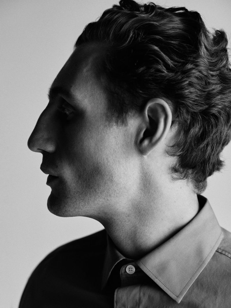 Black and white profile portrait of a man wearing a collared shirt against a light studio background.