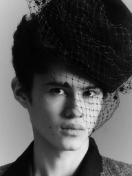 Black and white portrait of a young man wearing a black hat with birdcage netting veil draped over his face.