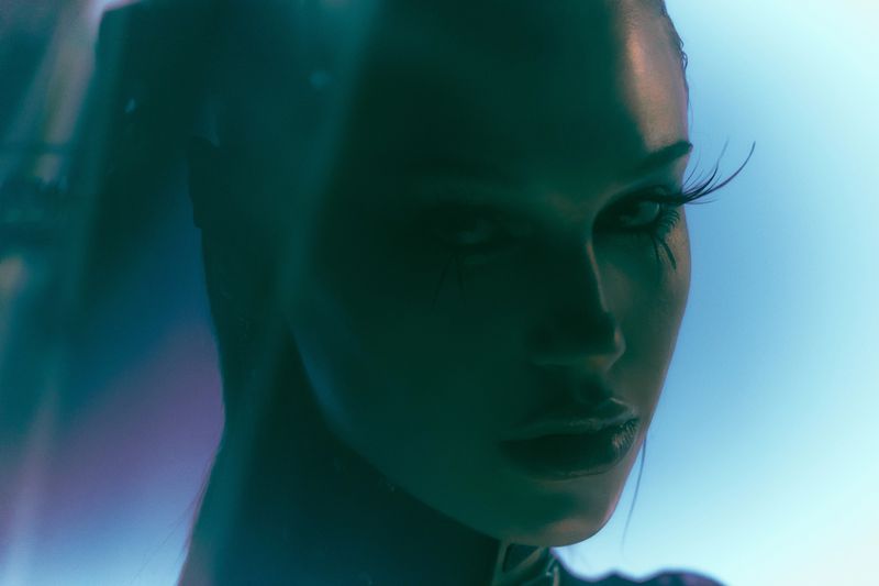 Close-up portrait of model Meredith Mickelson in shadow with dramatic eyelashes under cool cyan and blue lighting.