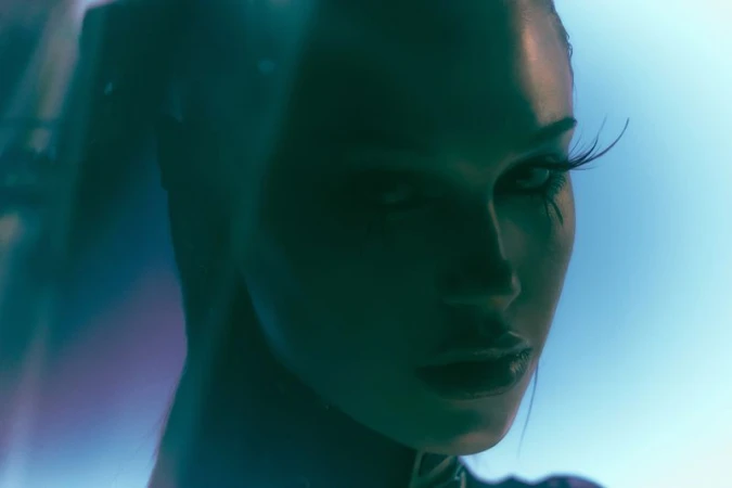 Close-up portrait of model Meredith Mickelson in shadow with dramatic eyelashes under cool cyan and blue lighting.