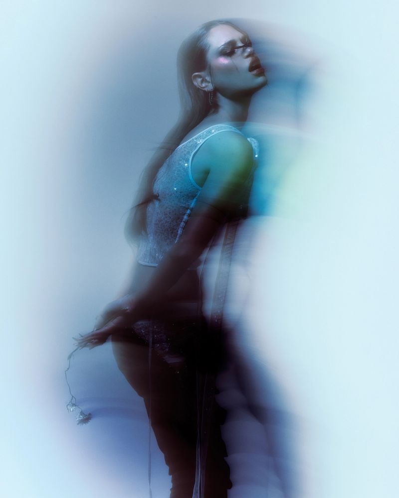 Meredith Mickelson poses in a shimmering light blue top with artistic motion blur against a cool-toned gradient background.