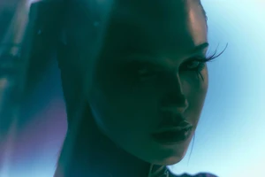 Close-up portrait of model Meredith Mickelson in shadow with dramatic eyelashes under cool cyan and blue lighting.