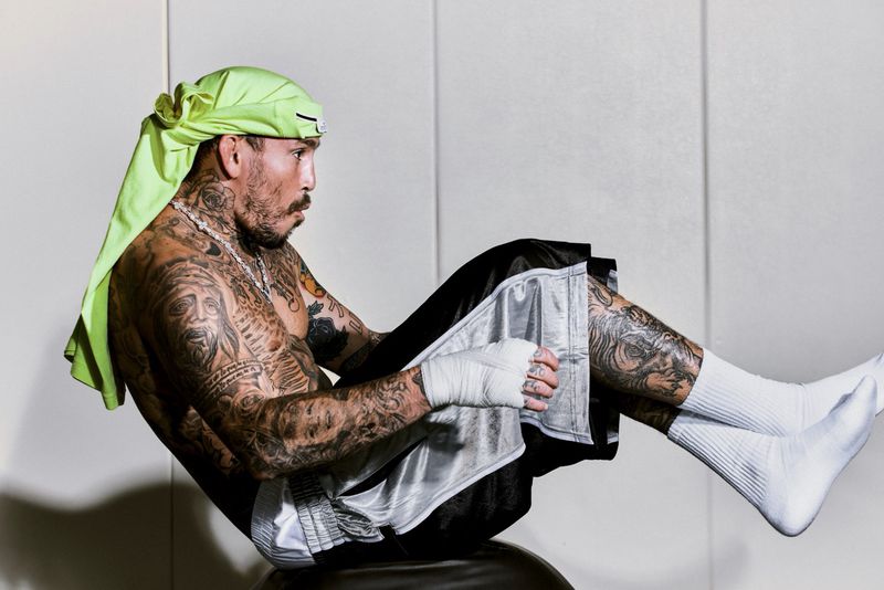 Marlon Chito Vera in a neon green headwrap and black athletic shorts doing an ab exercise against a plain studio wall.