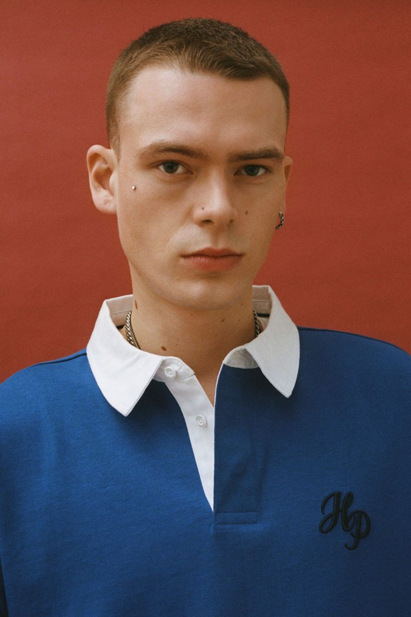 Model Zeph Daniels wearing a blue rugby shirt with a white collar against a warm red studio backdrop.