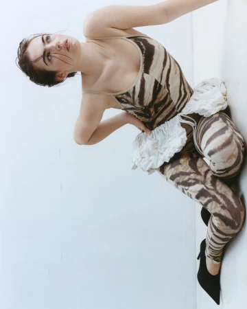 Stella Jones in a brown tiger-print jumpsuit and black heels posing against a white studio background.