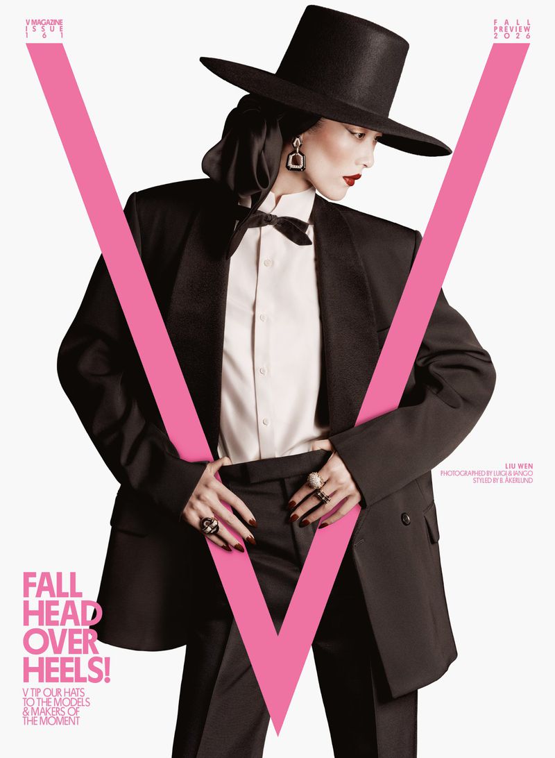 Model wearing a black wide-brim hat, white shirt, and black suit against a seamless white background for V Magazine.