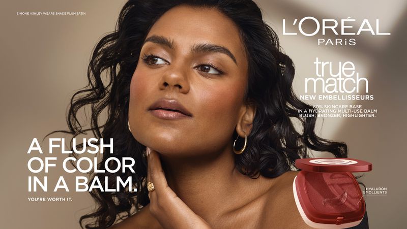 Simone Ashley with glowing makeup and wavy dark hair posing for L'Oreal Paris True Match balm campaign with product compact.