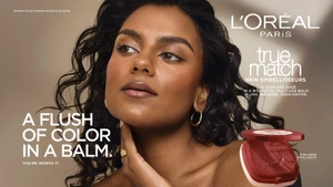 Simone Ashley with glowing makeup and wavy dark hair posing for L'Oreal Paris True Match balm campaign with product compact.